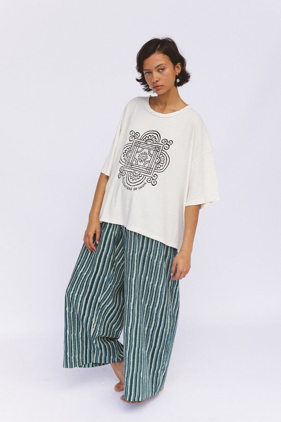 Shanti Tee White — side view against blue sky, white oversized cotton tee with charcoal mandala logo, relaxed oversized fit, paired with peony floral skirt | Daughters of India