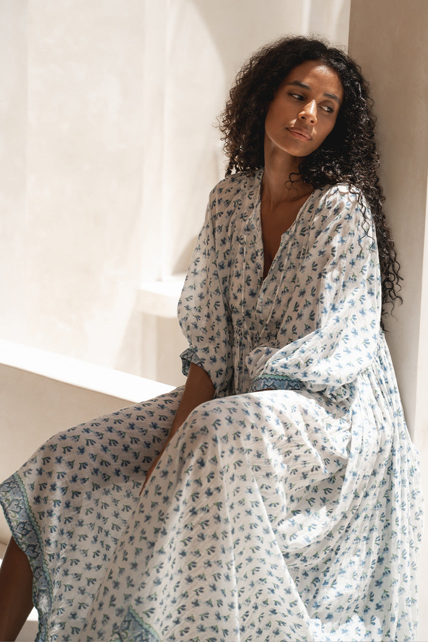 Daughters of India Kyra Maxi Dress in Azure — seated against cream pillar, draped skirt, blue floral block print cotton