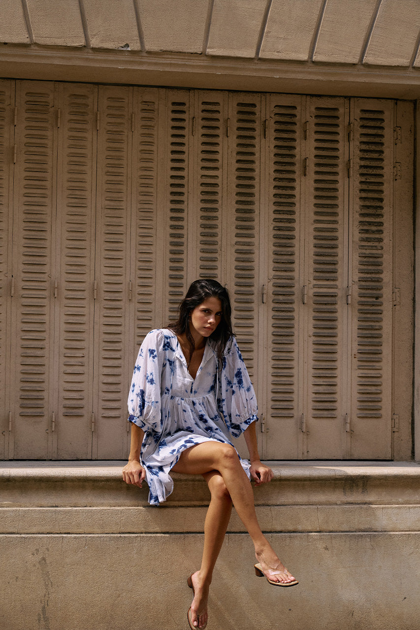 Kyra Mini Dress Deep Sea — seated pose against shuttered window, deep sea shibori tie-dye cotton mini dress, relaxed European street style | Daughters of India