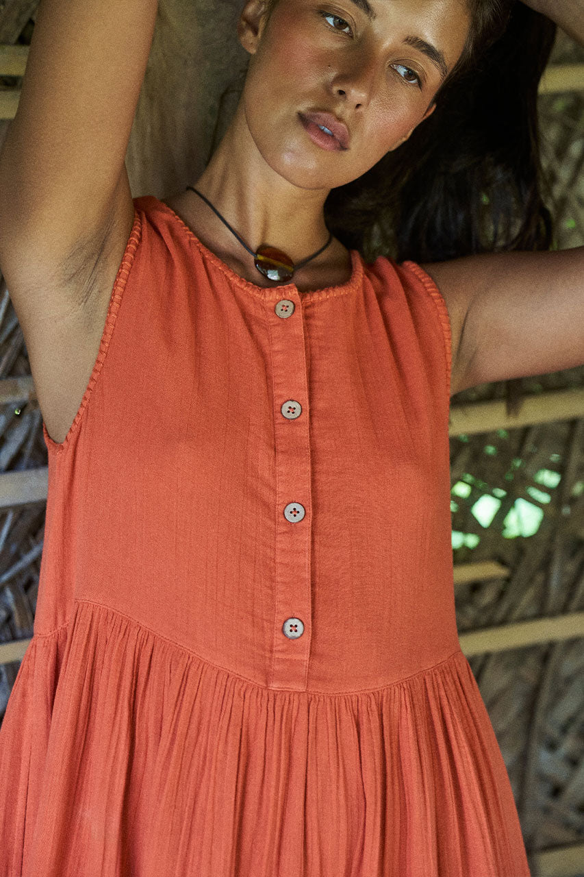 Nadi Dress Terracotta — close-up of wooden button front and gathered waist detail, terracotta double gauze cotton texture, rustic bamboo setting | Daughters of India