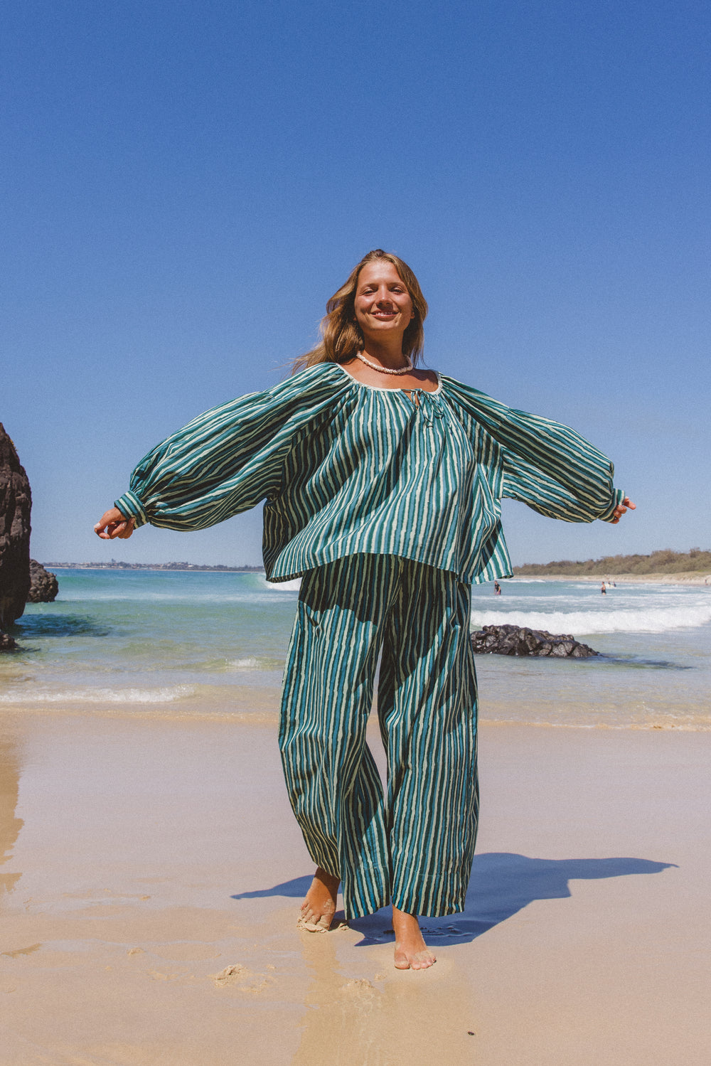 Ria Blouse Cyan Candy — full length beach walking shot, model barefoot on wet sand wearing cyan and dark stripe hand block print cotton blouse, relaxed silhouette, artisan Jaipur India | Daughters of India