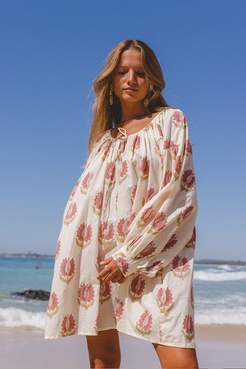 Ria Mini Dress Strawberry Cream — mid-body beach front view, model wearing strawberry cream floral hand block print cotton mini dress with ocean backdrop, relaxed A-line fit, artisan Jaipur India | Daughters of India