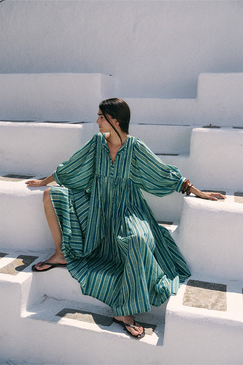 Woman sitting on white steps wearing the Daughters of India Kyra Maxi Dress in Spearmint, a flowing green striped cotton maxi dress with billowed sleeves